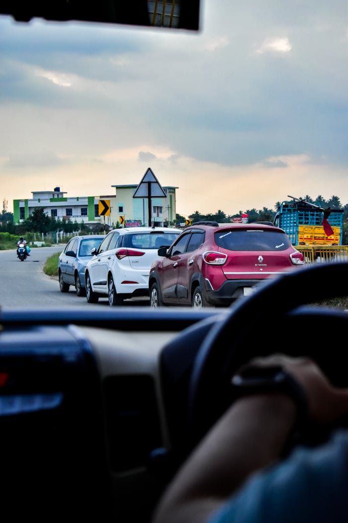 Interior view of a car driving on a road with multiple vehicles ahead. Scenic cloudy sky visible.